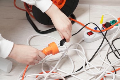 Photo of Woman putting plug into extension cord reel indoors, closeup