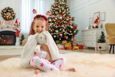 Photo of Cute little girl with toy bunny in room decorated for Christmas