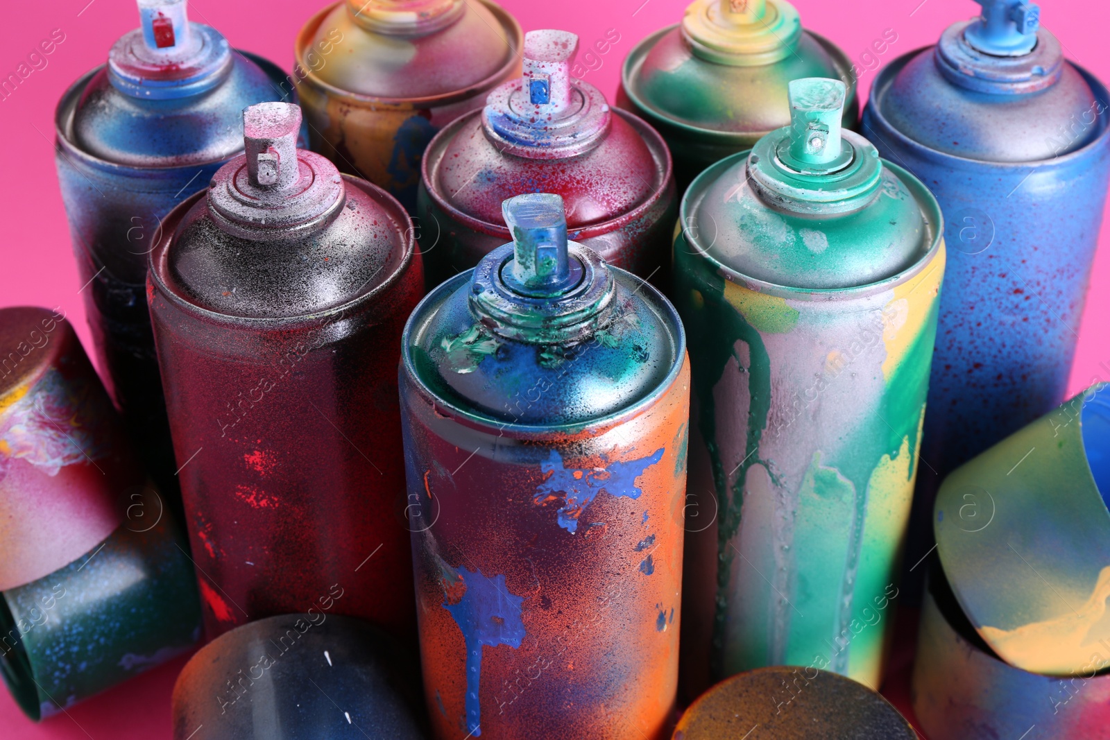 Photo of Many spray paint cans with caps on pink background