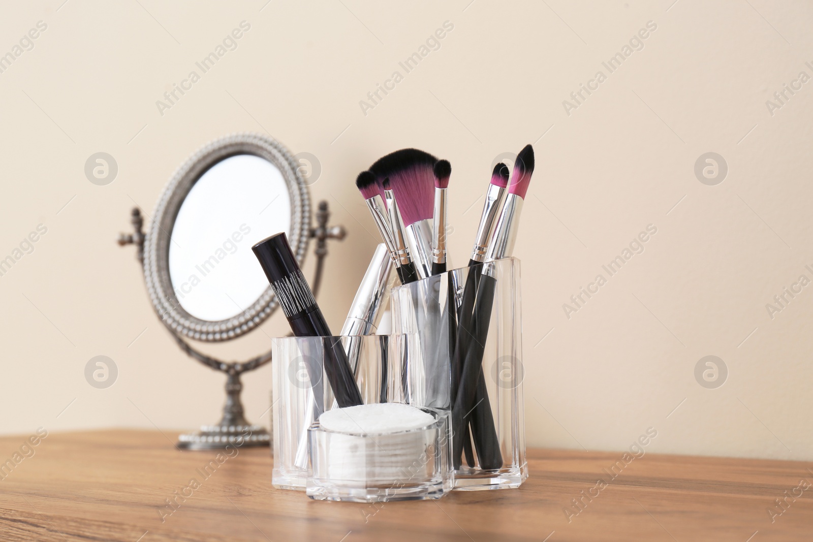 Photo of Organizer with cosmetic products for makeup and mirror on table against light wall