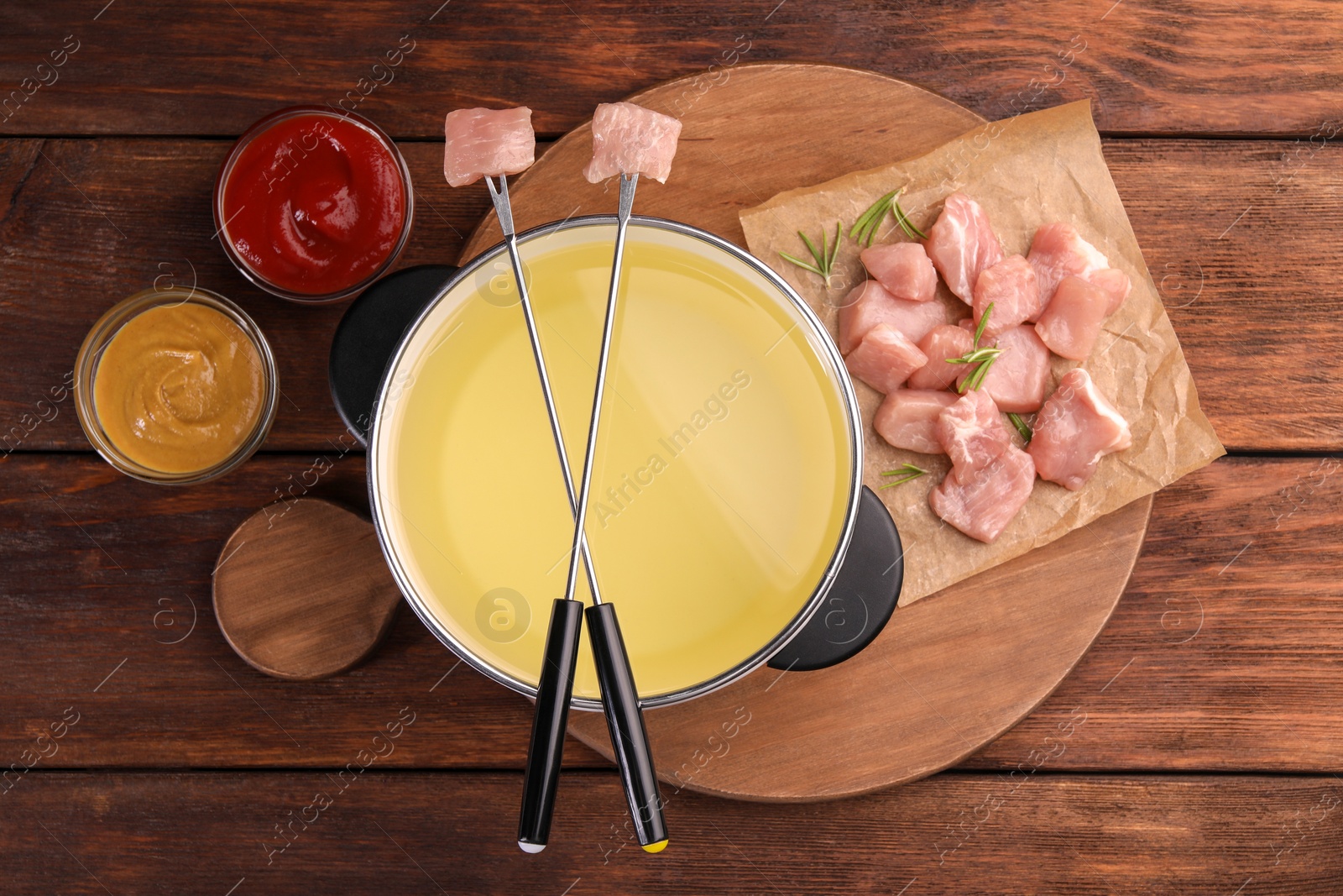 Photo of Fondue pot, forks with pieces of raw meat and sauces on wooden table, flat lay