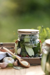 Jar of delicious pickled cucumbers and ingredients on wooden table against blurred background