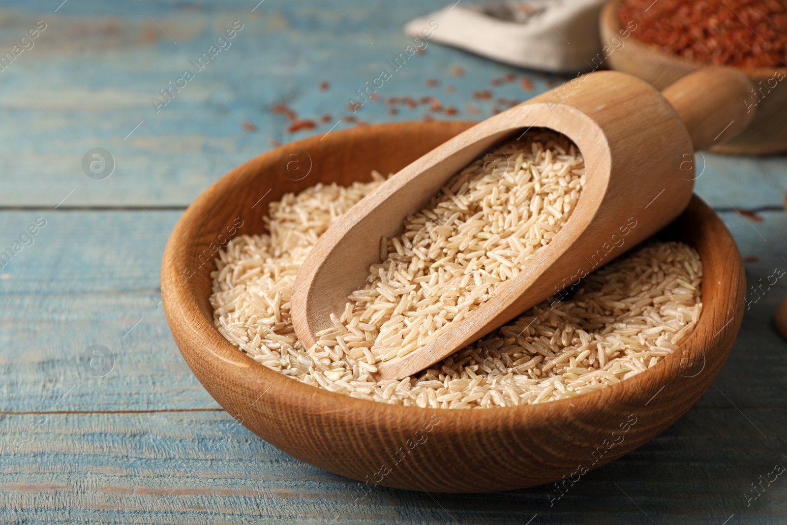 Photo of Uncooked brown rice in scoop and bowl on table