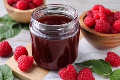 Photo of Delicious raspberry jam, fresh berries and green leaves on table