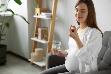 Beautiful pregnant woman holding pill and glass with water at home