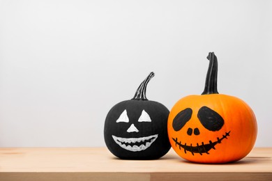 Photo of Halloween celebration. Pumpkins with drawn faces on wooden table against light grey background, space for text