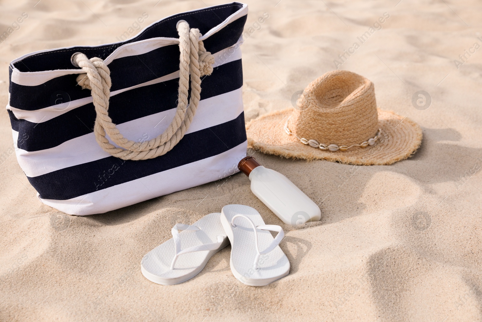 Photo of Beach bag, flip flops, sunscreen and hat on sand
