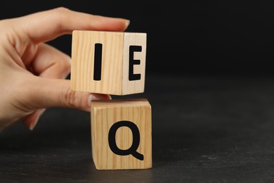 Photo of Woman turning cube with letters E and I above Q at black slate table, closeup. Space for text