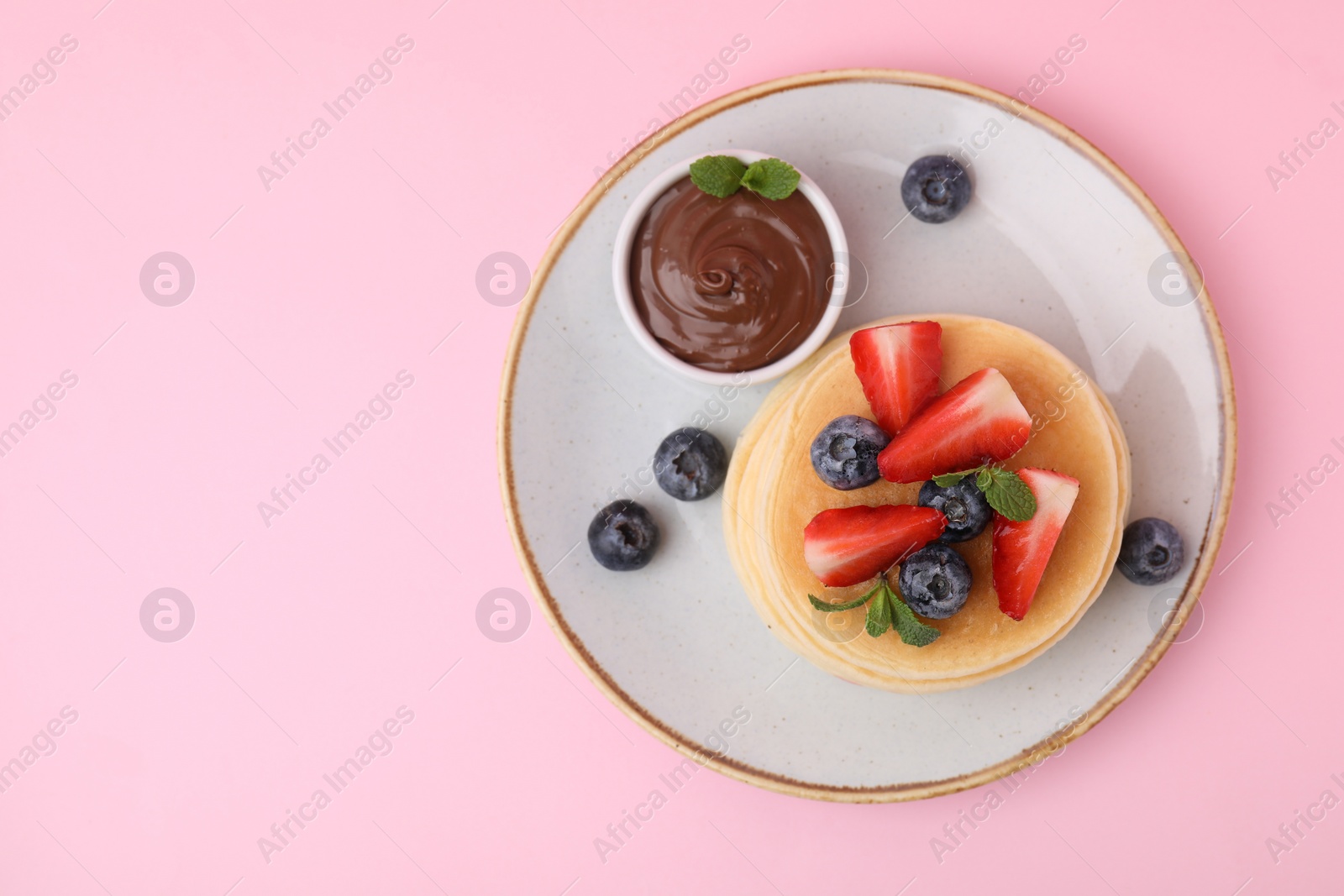 Photo of Delicious pancakes with strawberries, blueberries, mint and chocolate sauce on pink background, top view. Space for text