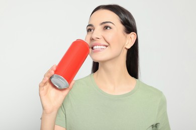 Beautiful happy woman holding red beverage can on light grey background