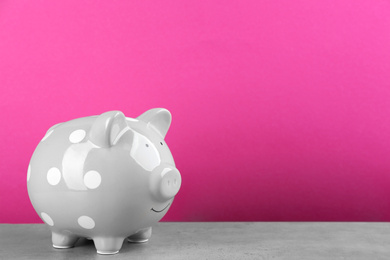 Grey piggy bank on light grey table against pink background. Space for text
