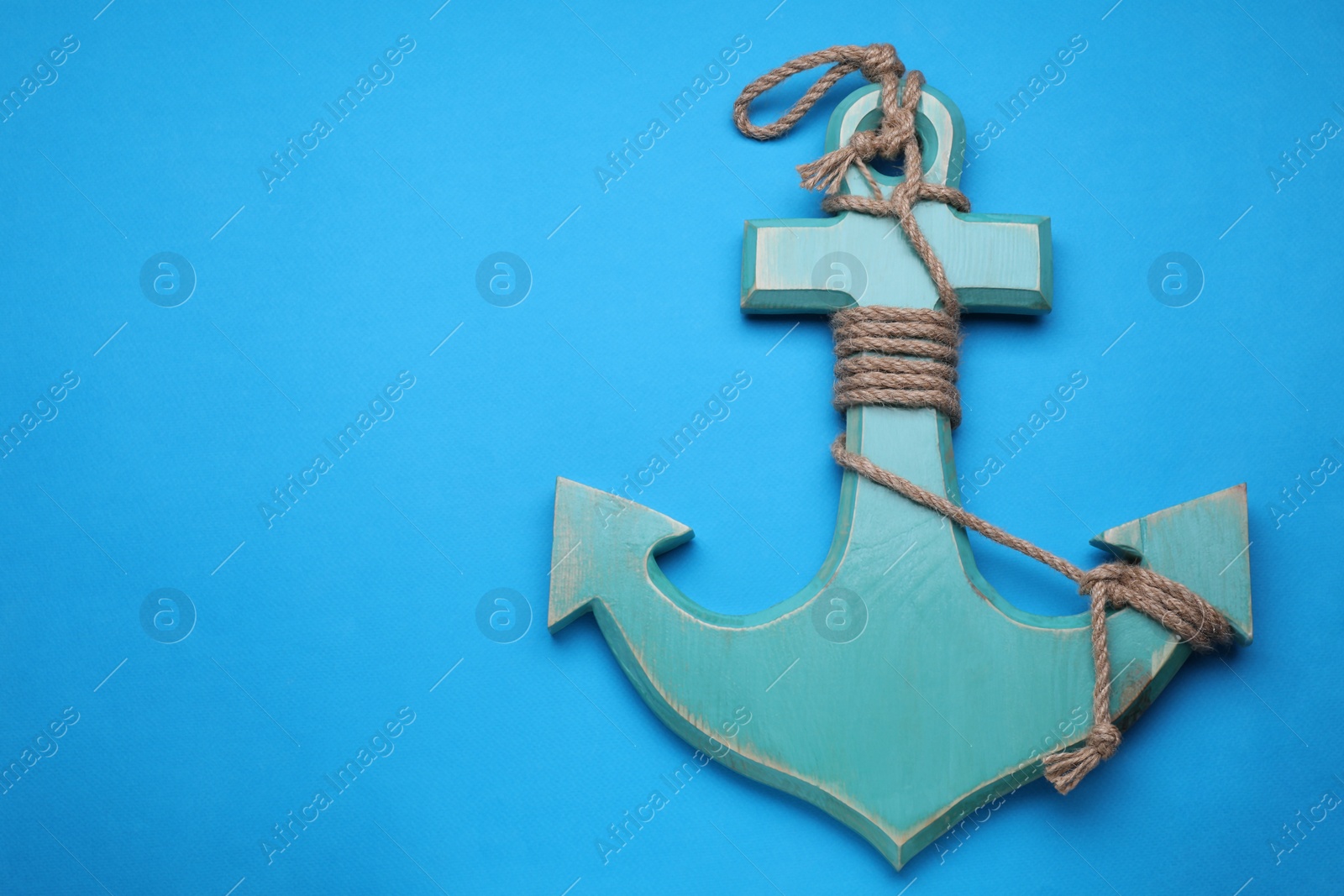 Photo of Wooden anchor with hemp rope on light blue background, top view. Space for text