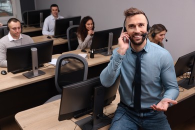 Photo of Handsome call center operator with headset and his colleagues working in office, above view