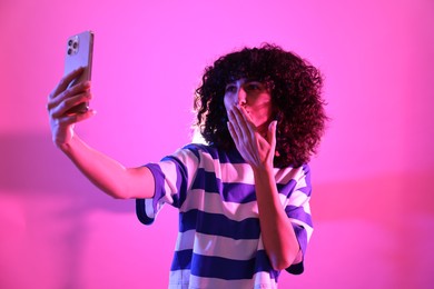 Photo of Beautiful young woman taking selfie on color background in neon lights