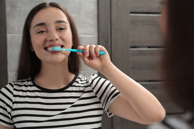 Photo of Young woman brushing her teeth with plastic toothbrush near mirror in bathroom