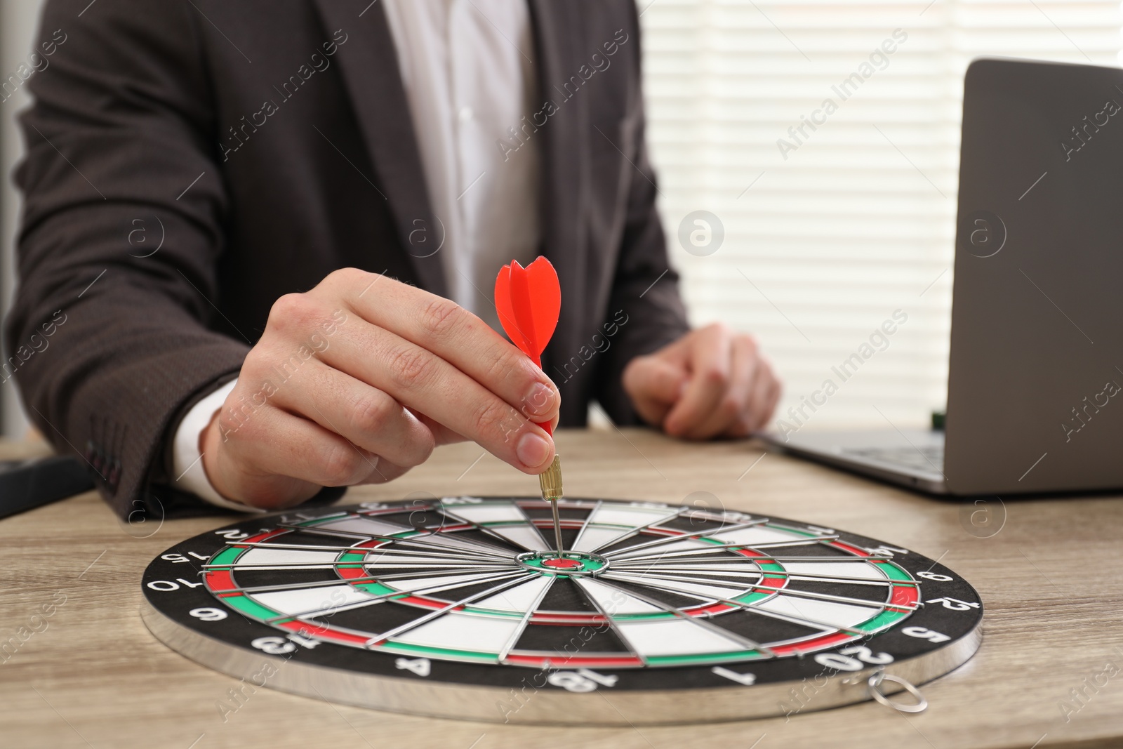 Photo of Business targeting concept. Man with dart aiming at dartboard at wooden table indoors, closeup