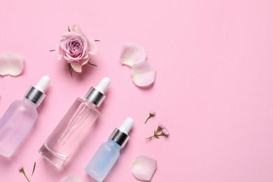 Photo of Bottles of cosmetic serums, flowers and petals on pink background, flat lay. Space for text