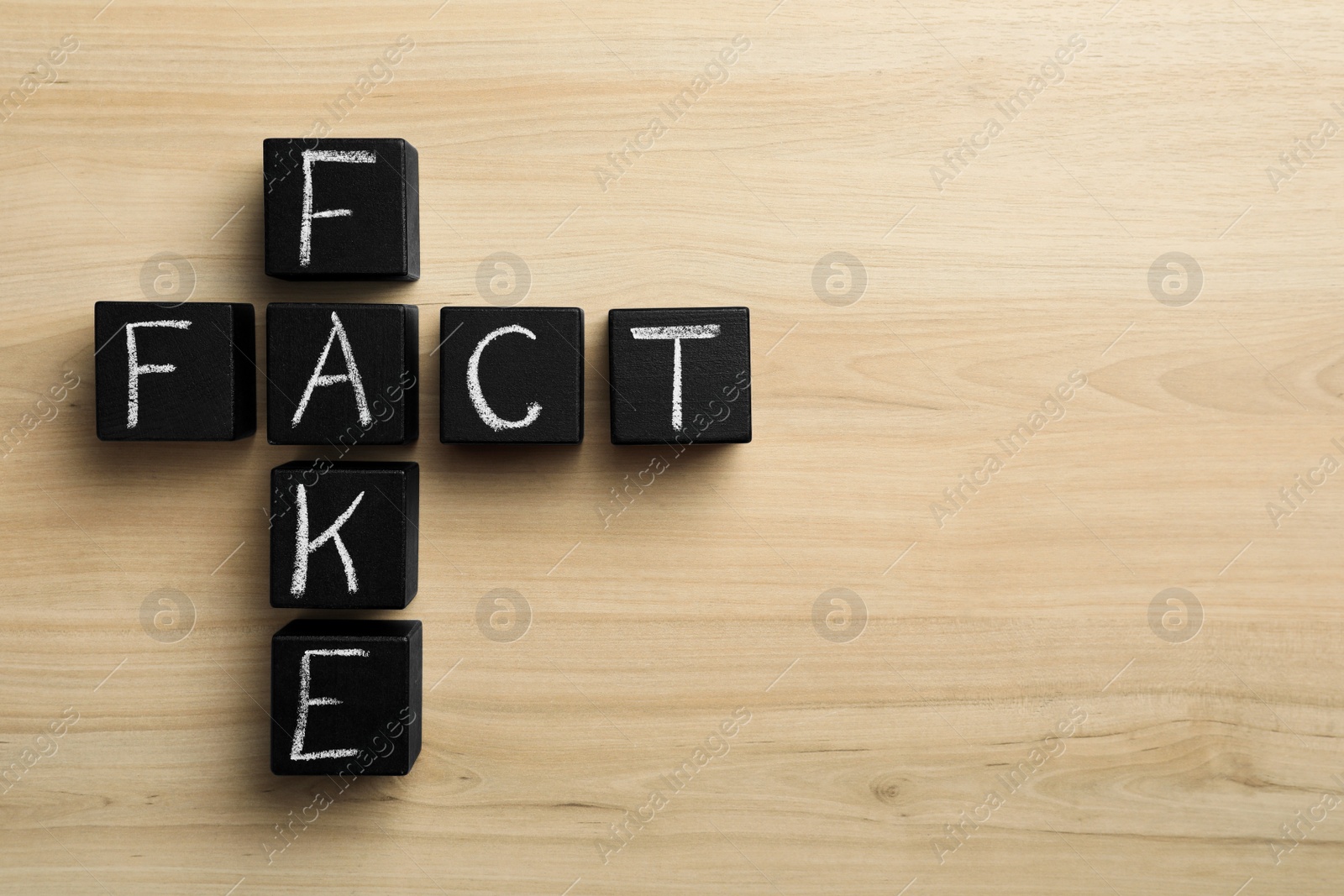 Photo of Words FAKE and FACT made with black cubes on wooden table, flat lay. Space for text