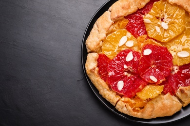 Photo of Tasty galette with citrus fruits on dark grey table, top view