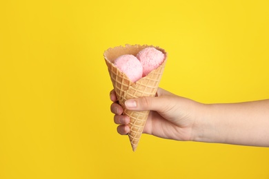 Photo of Woman holding delicious ice cream in wafer cone on yellow background, closeup