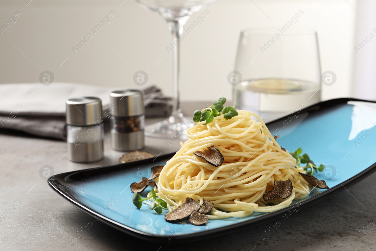 Photo of Delicious pasta with truffle slices and microgreens served on light grey table, space for text