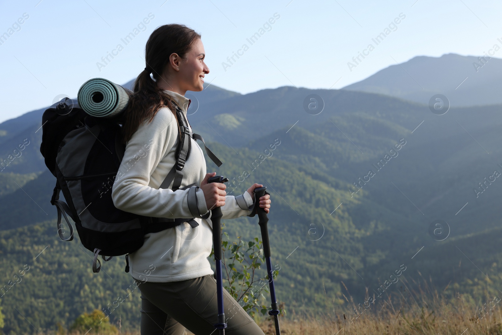 Photo of Tourist with backpack and trekking poles hiking through mountains, space for text