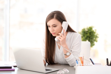 Photo of Young woman talking on phone at workplace