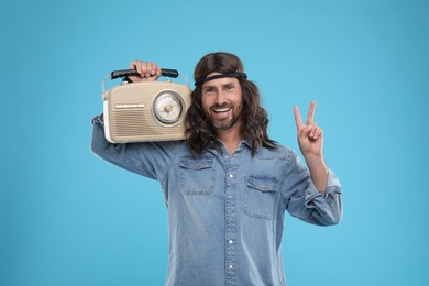 Photo of Stylish hippie man with retro radio receiver showing V-sign on light blue background