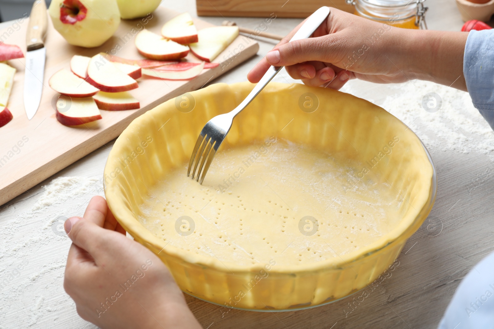 Photo of Woman making holes in raw dough with fork at white wooden table, closeup. Baking apple pie