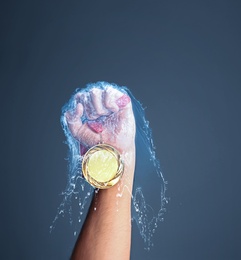 Image of Winner raising hand with gold medal through water splash on dark grey background, closeup
