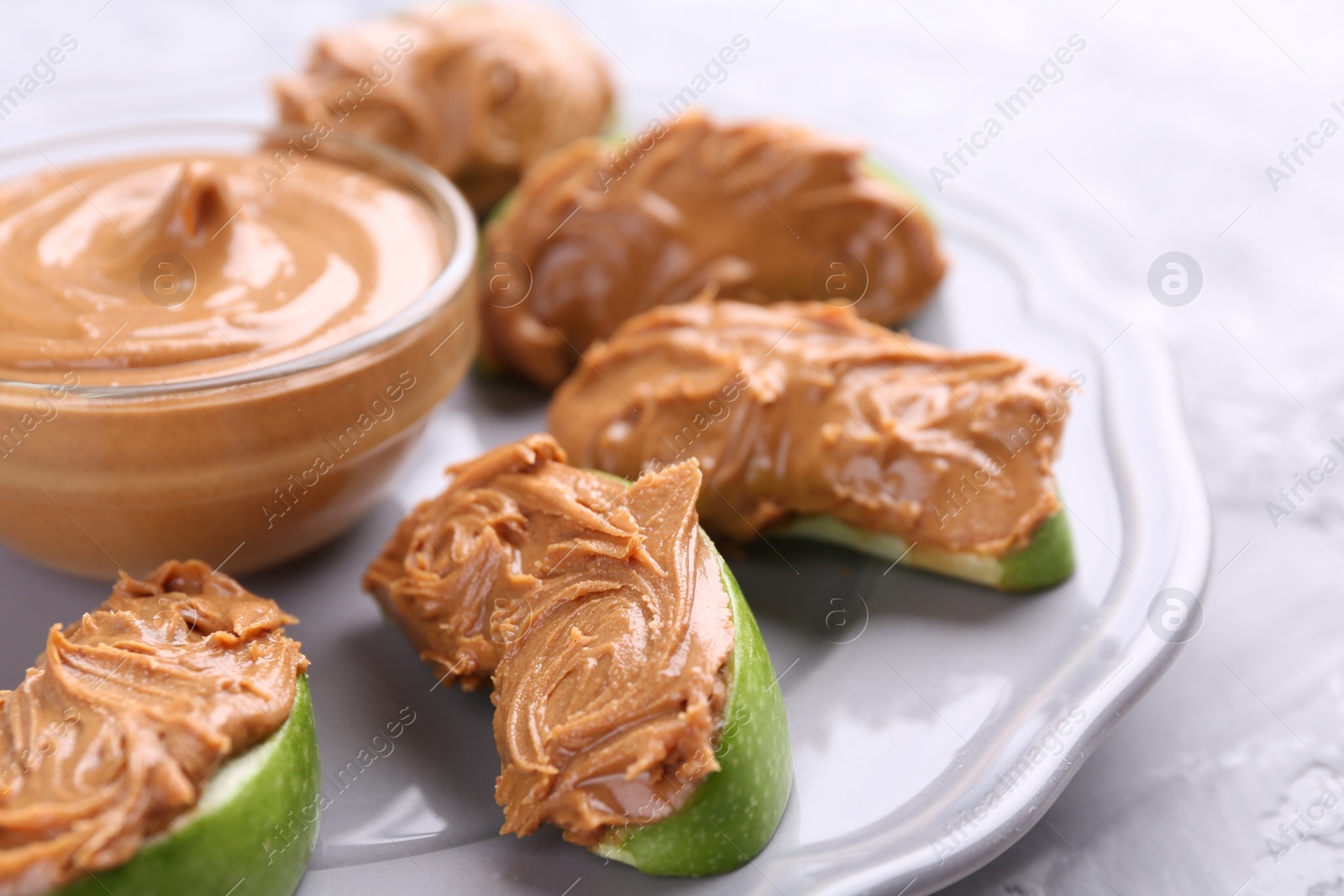 Photo of Slices of fresh green apple with peanut butter on light textured table, closeup