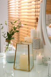 Photo of Burning scented candles and bouquet on dressing table indoors