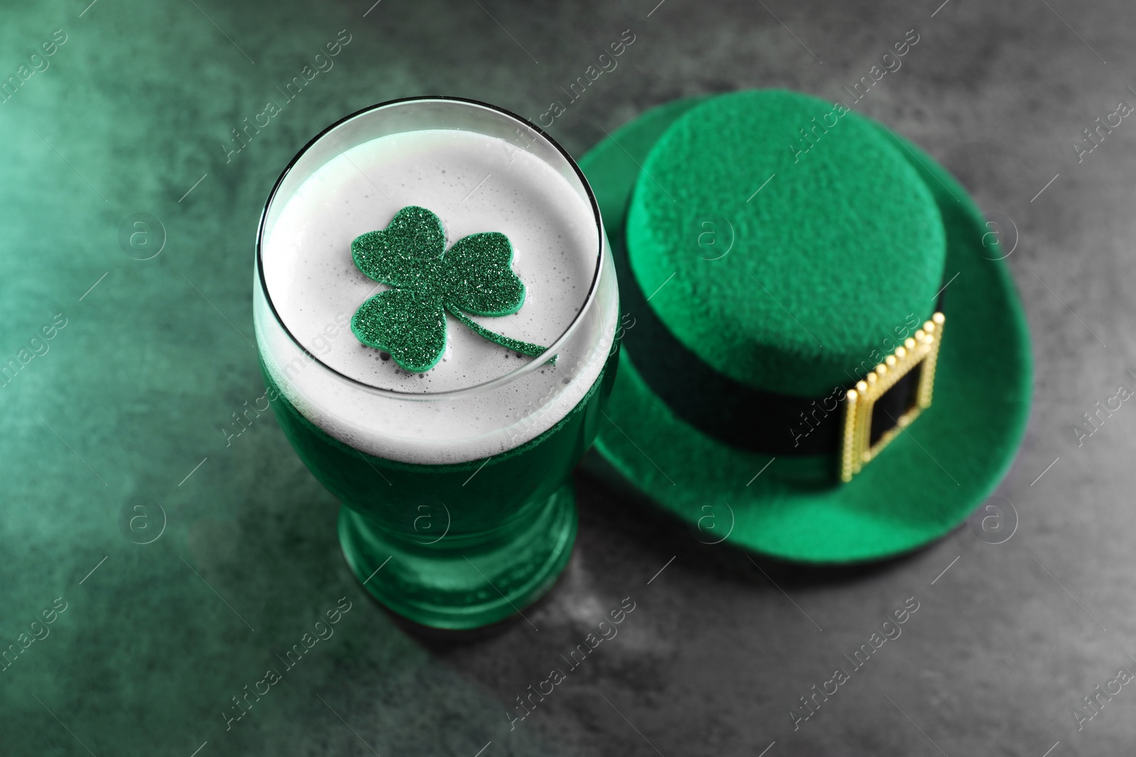 Photo of St. Patrick's day celebration. Green beer with decorative clover leaf and leprechaun hat on grey table