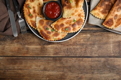 Photo of Delicious fried chebureki with ketchup and onion served on wooden table, flat lay. Space for text