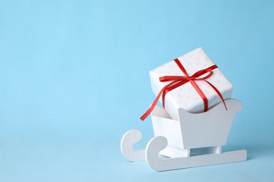 Photo of White wooden sleigh with Christmas gift box on light blue background, space for text