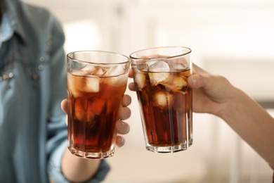 Women holding glasses of cola with ice on blurred background, closeup