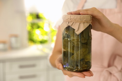 Photo of Woman holding jar of pickled cucumbers indoors, closeup