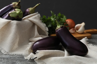 Photo of Ripe purple eggplants and napkin on grey table