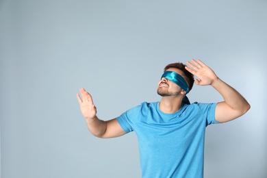 Young man with light blue blindfold on grey background