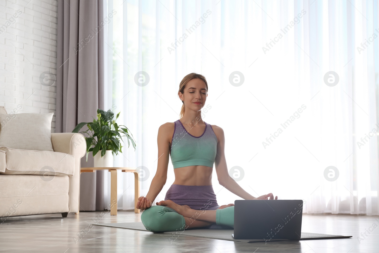 Photo of Woman having online video class via laptop at home. Distance yoga course during coronavirus pandemic