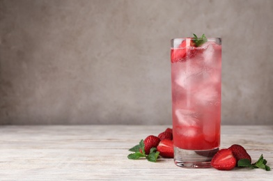 Photo of Glass of refreshing drink with strawberry and mint on light wooden table against grey background, space for text