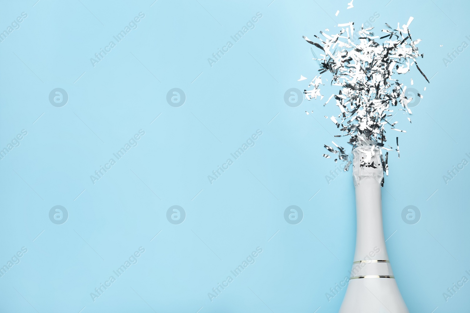 Photo of Flat lay composition with confetti and bottle of champagne on light blue background. Space for text