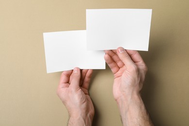 Man holding flyers on light brown background, top view. Mockup for design