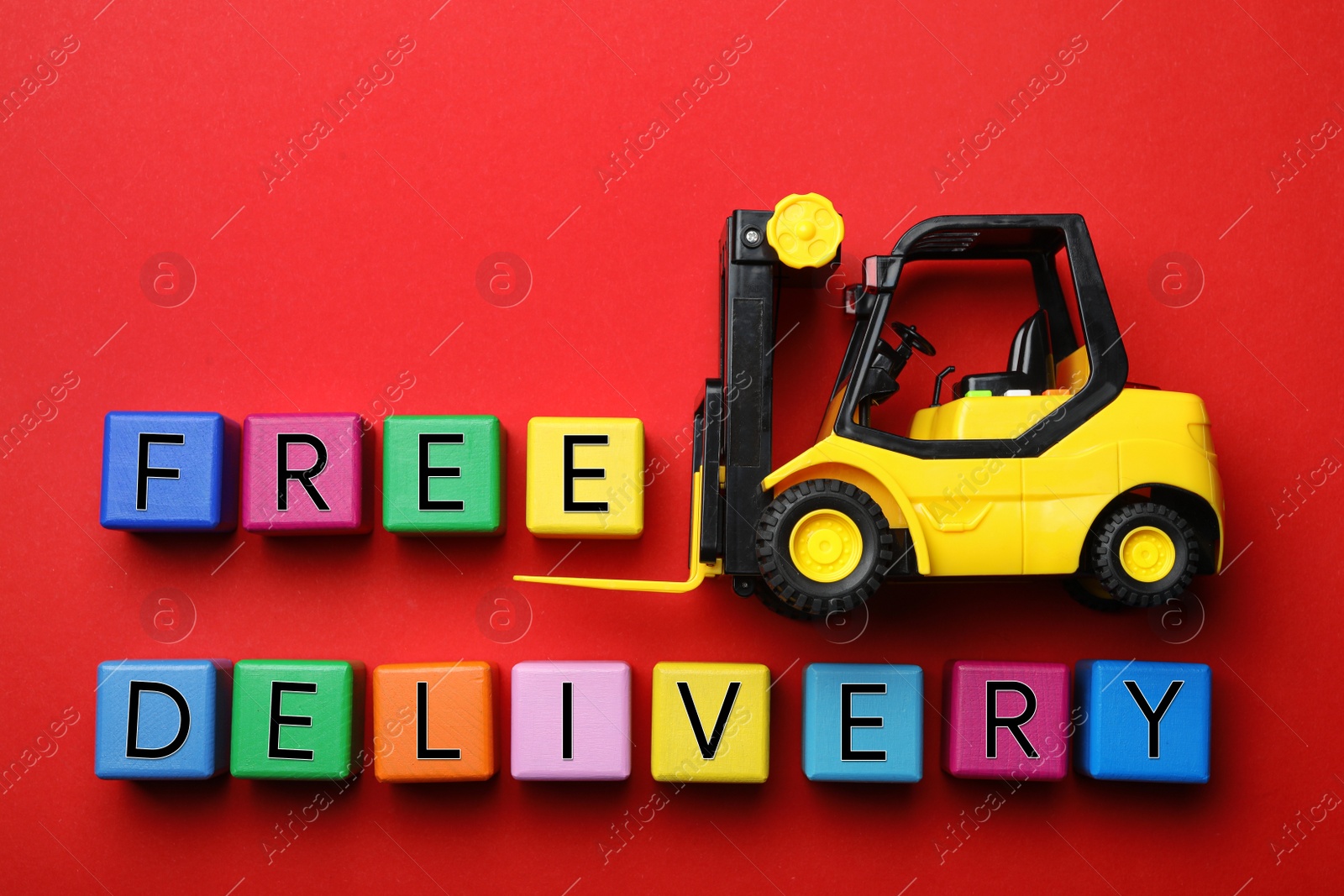 Photo of Flat lay composition of toy forklift and words FREE DELIVERY on red background. Logistics and wholesale concept