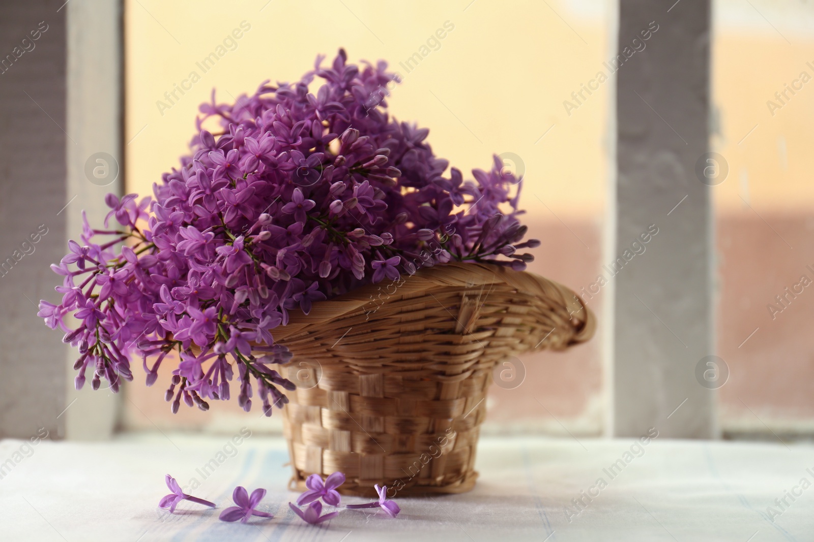 Photo of Beautiful lilac flowers in wicker basket on window sill indoors