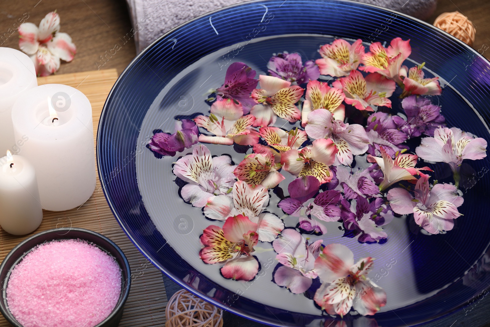 Photo of Bowl of water with flowers, sea salt and candles on table. Spa treatment