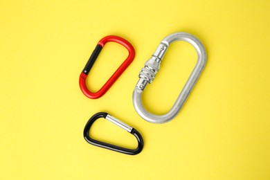 Metal carabiners on yellow background, flat lay