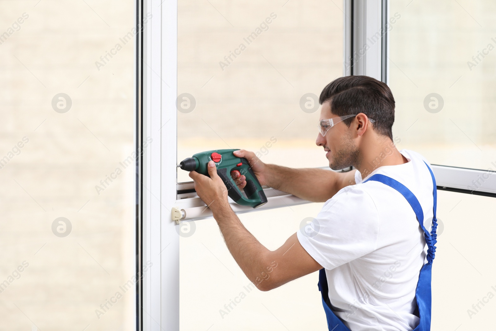 Photo of Construction worker repairing plastic window with electric screwdriver indoors