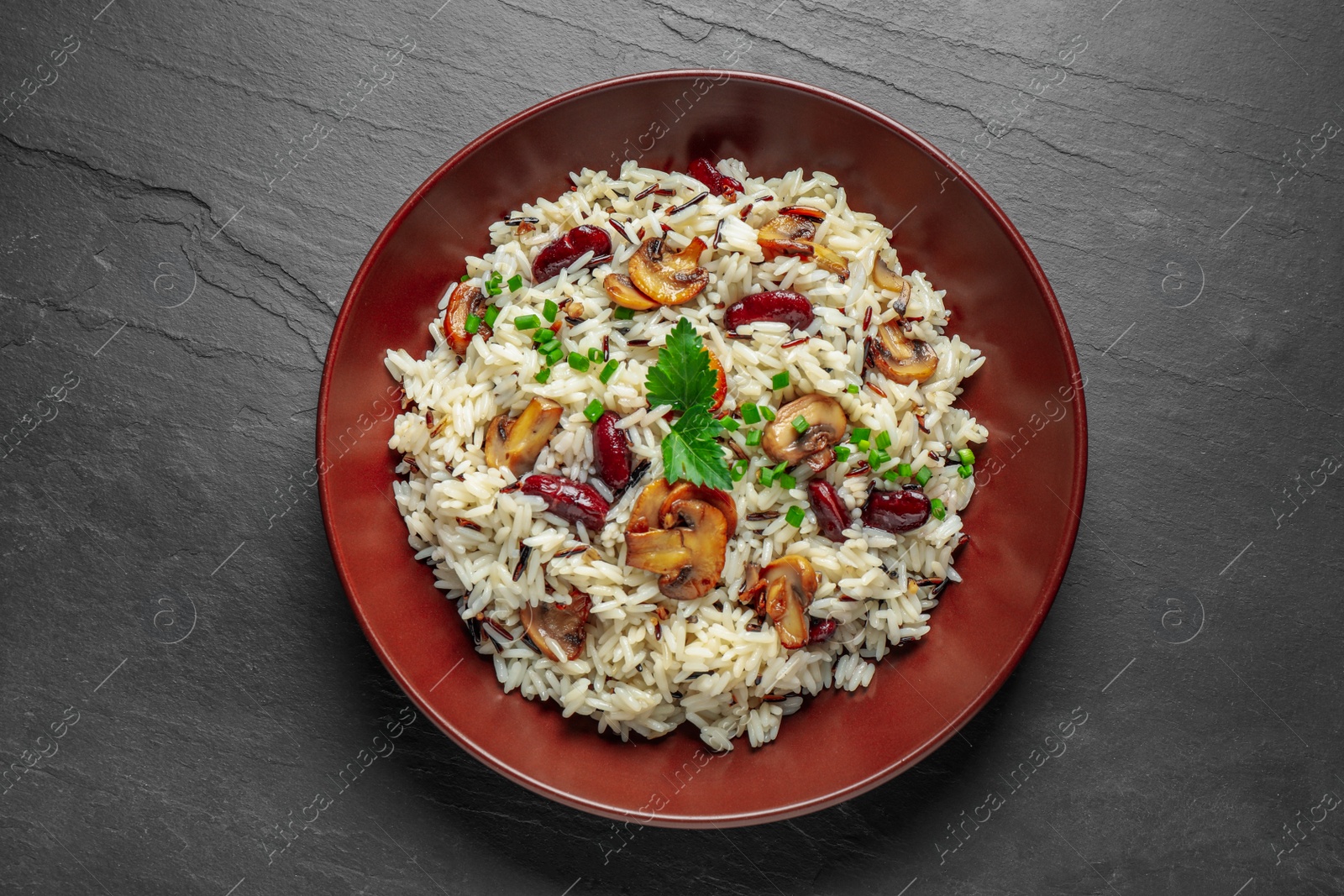 Photo of Delicious rice pilaf with mushrooms and beans on black table, top view