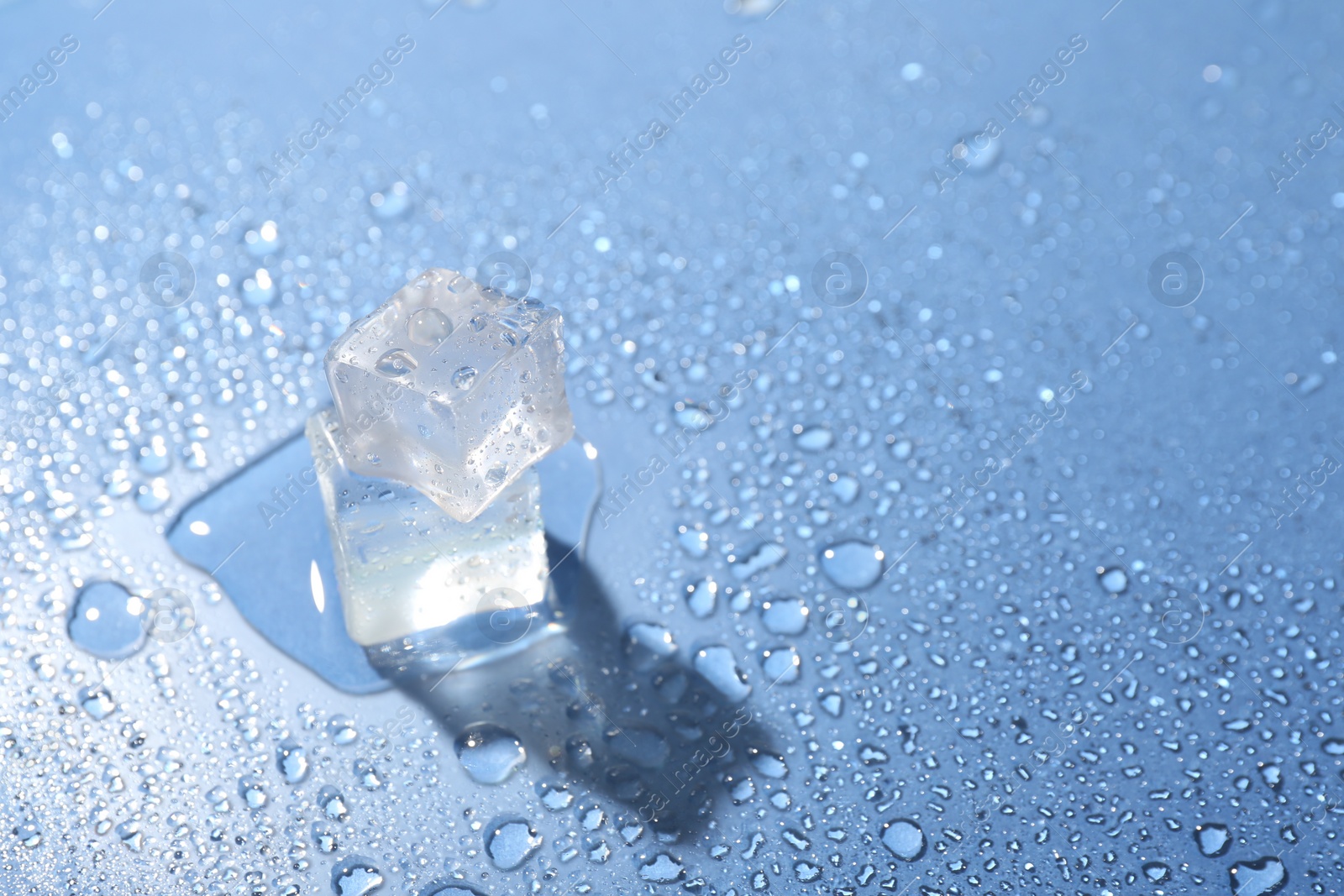 Photo of Melting ice cubes and water drops on light blue background, closeup. Space for text